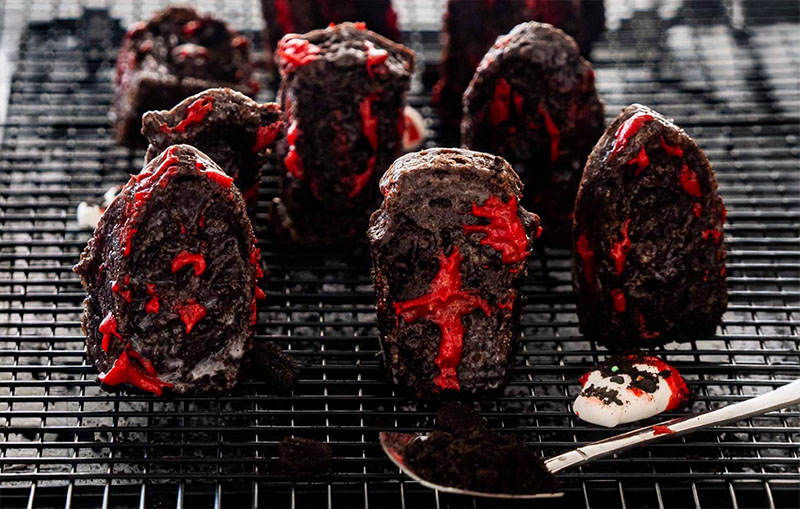 Tombstone-shaped chocolate cakes with red icing details, a gory Halloween baking idea.