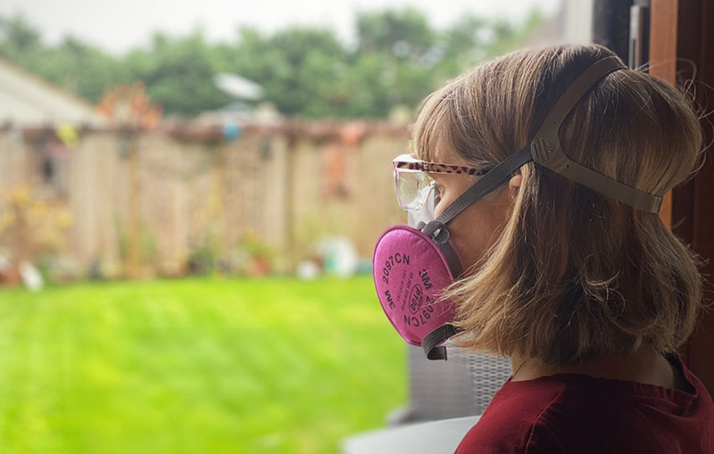 Crafter standing by open window, using mask for air quality protection during resin crafting.