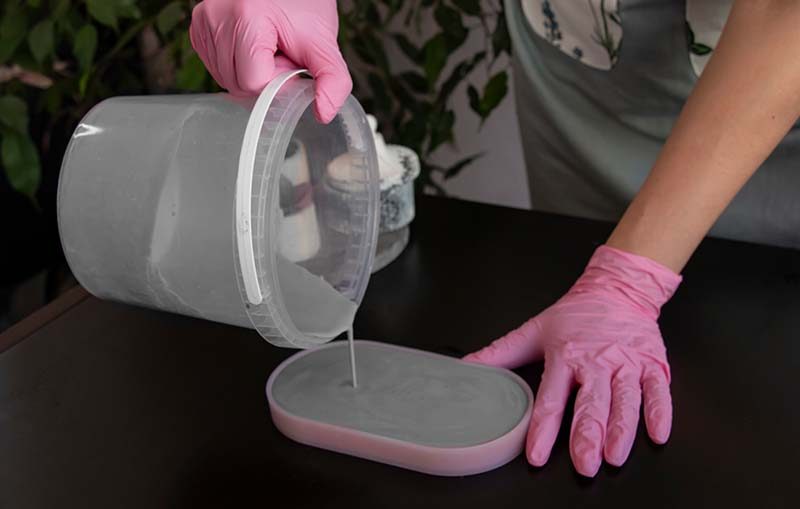 Pouring liquid concrete into a rectangular pink silicone mold, showcasing the flexibility of 'Silicone Molds with Concrete