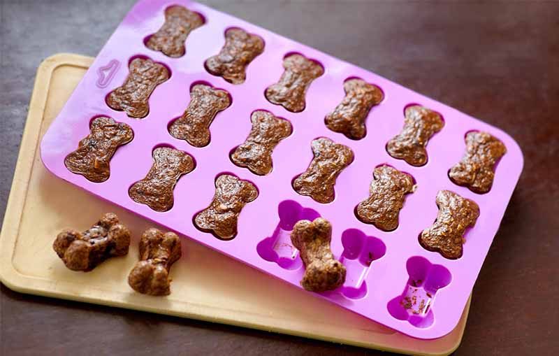 Cooking the homemade biscuits for dogs, bone-shaped in silicone mold, taken out of the oven. Dog treats from liver and carrot.